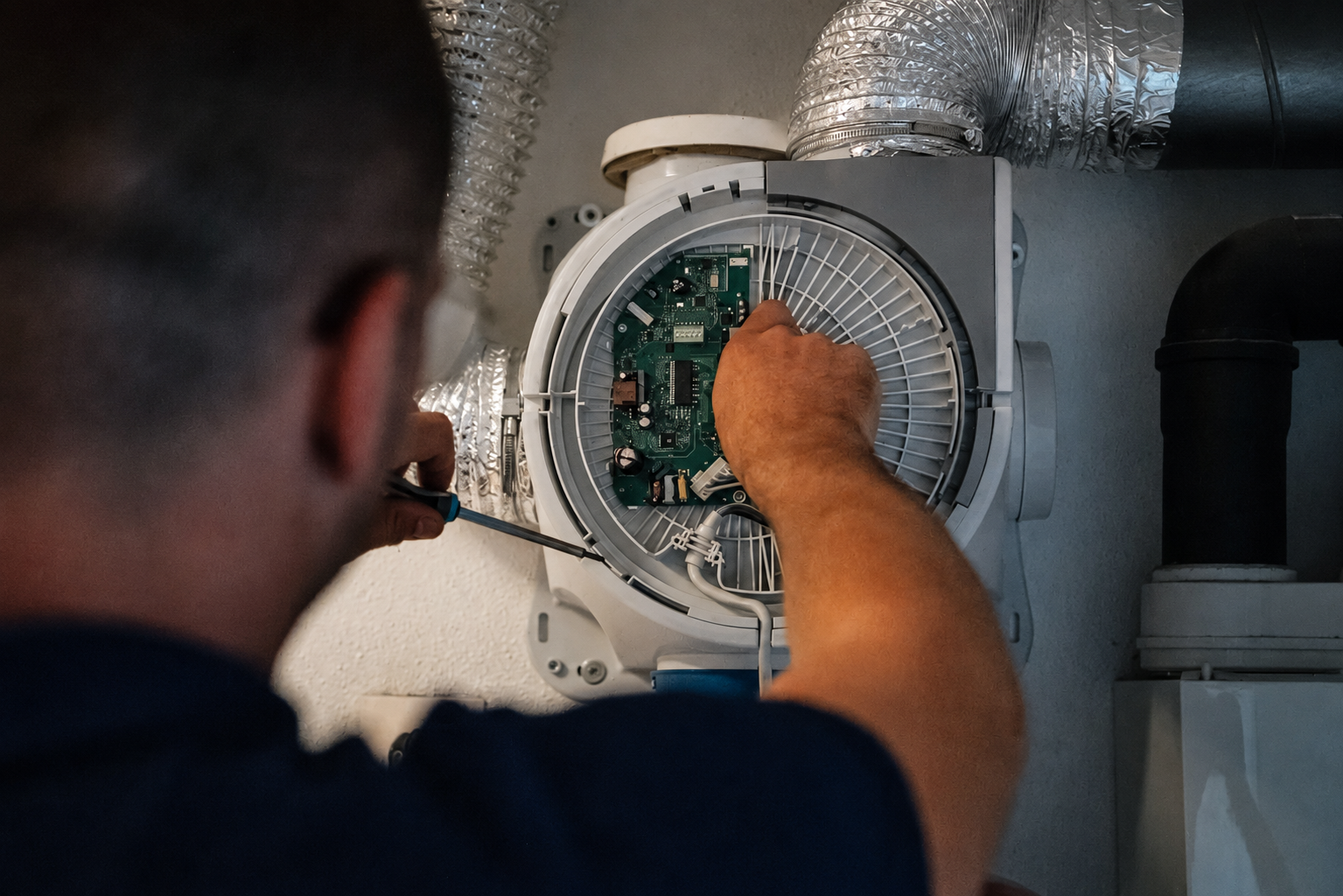 Monteur opent en herstelt een mechanische ventilatiebox met een schroevendraaier